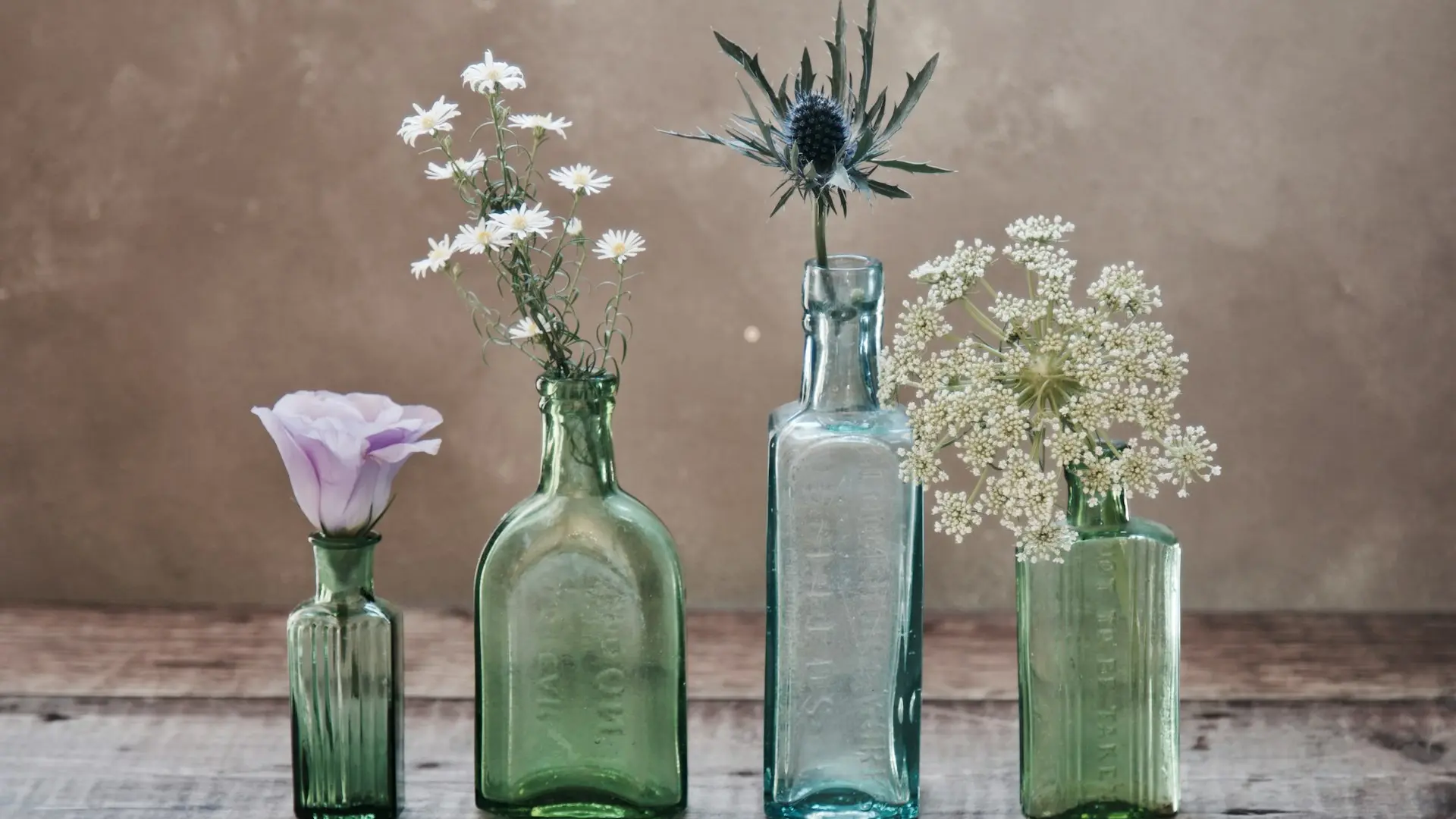 three green and one blue glass vases with flowers inside